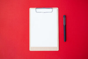 Top view of clipboard and pen on a red background.