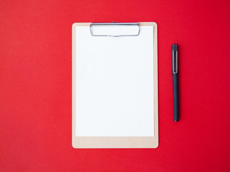 Top view of clipboard and pen on a red background.
